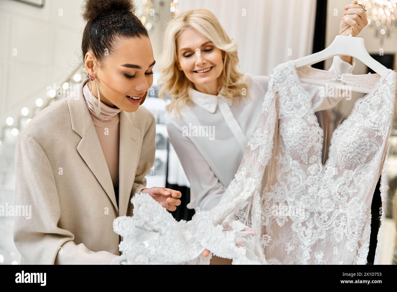 Two women admiring a white gown on a hanger in a bridal shop. The bride-to-be and shop assistant are discussing the dress. Stock Photo