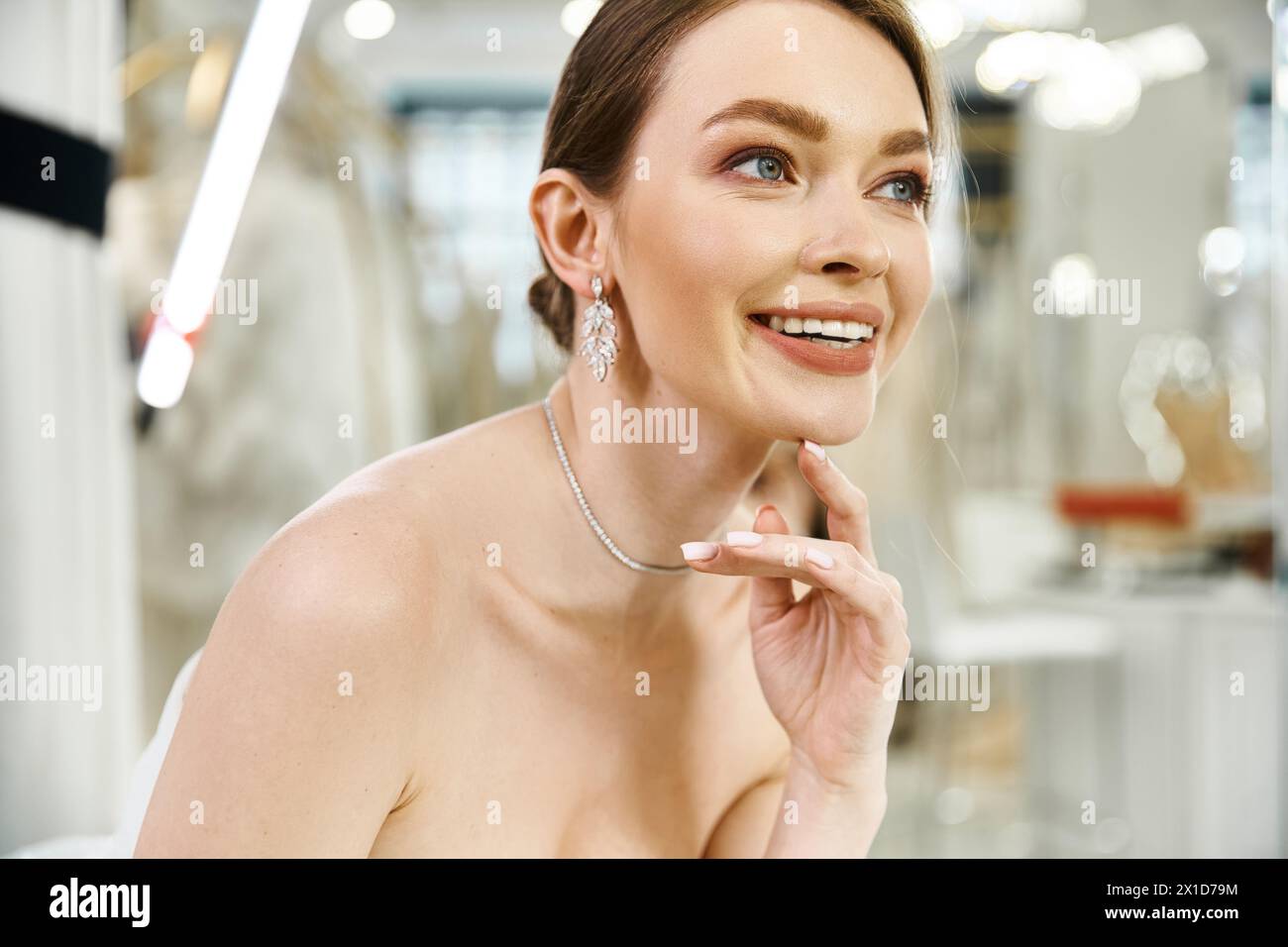 A young, beautiful brunette bride poses elegantly in a white dress in a wedding salon, exuding grace and poise. Stock Photo