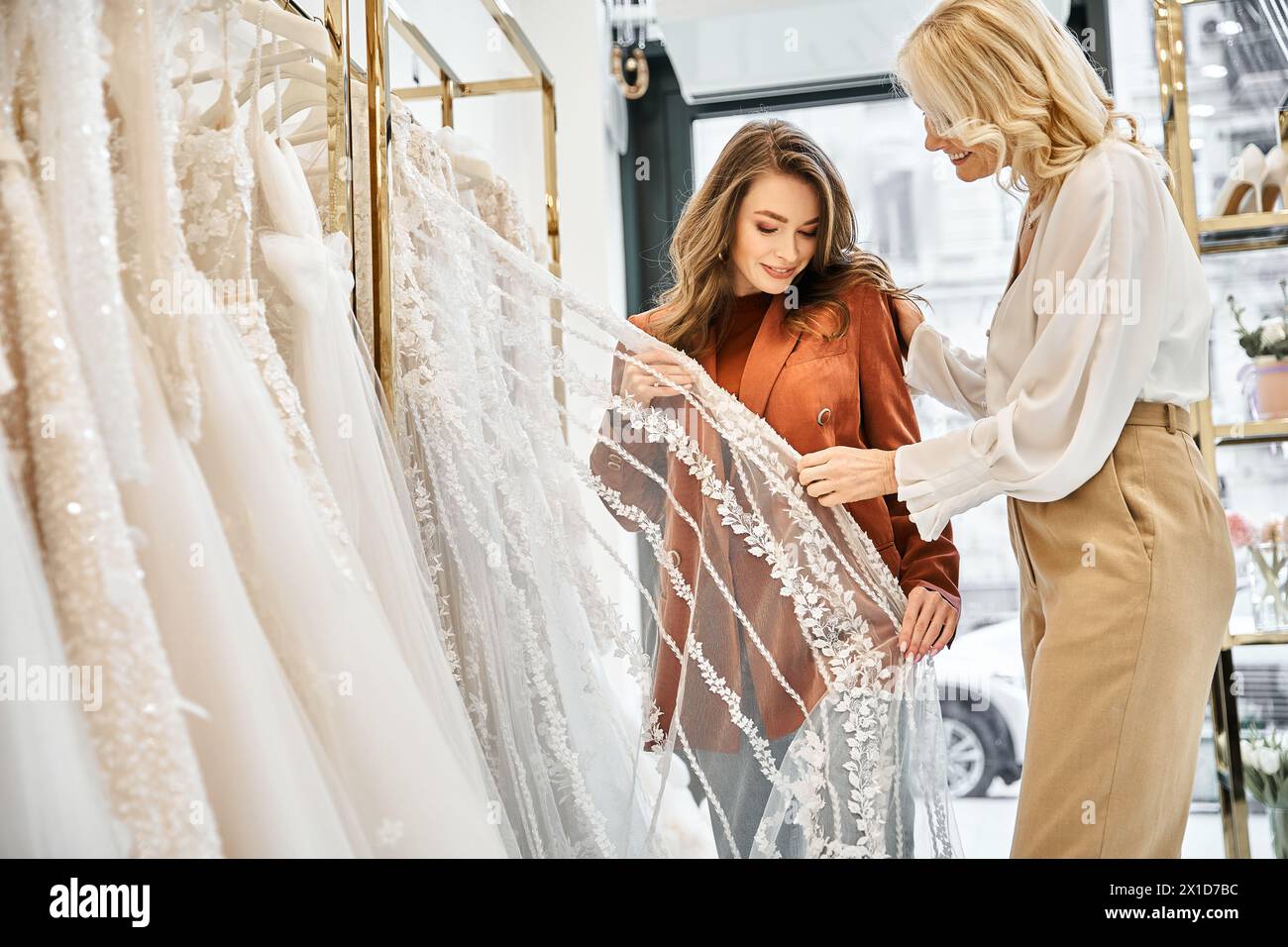 Two women, a young bride and her mother, admiring wedding dresses in a bridal store with excitement and anticipation. Stock Photo