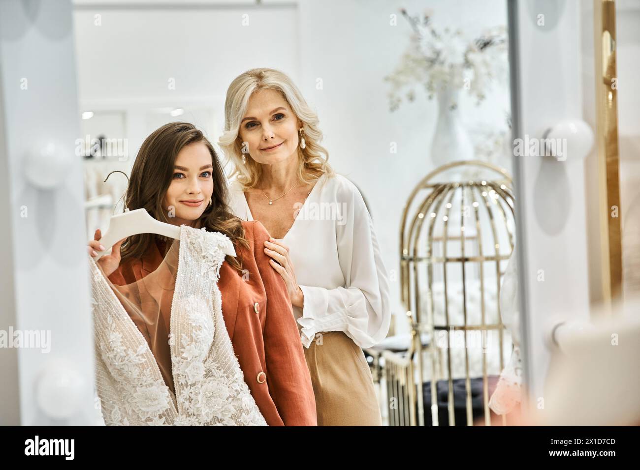 A young beautiful bride and her mother stand together in a room, immersed in wedding shopping preparations. Stock Photo