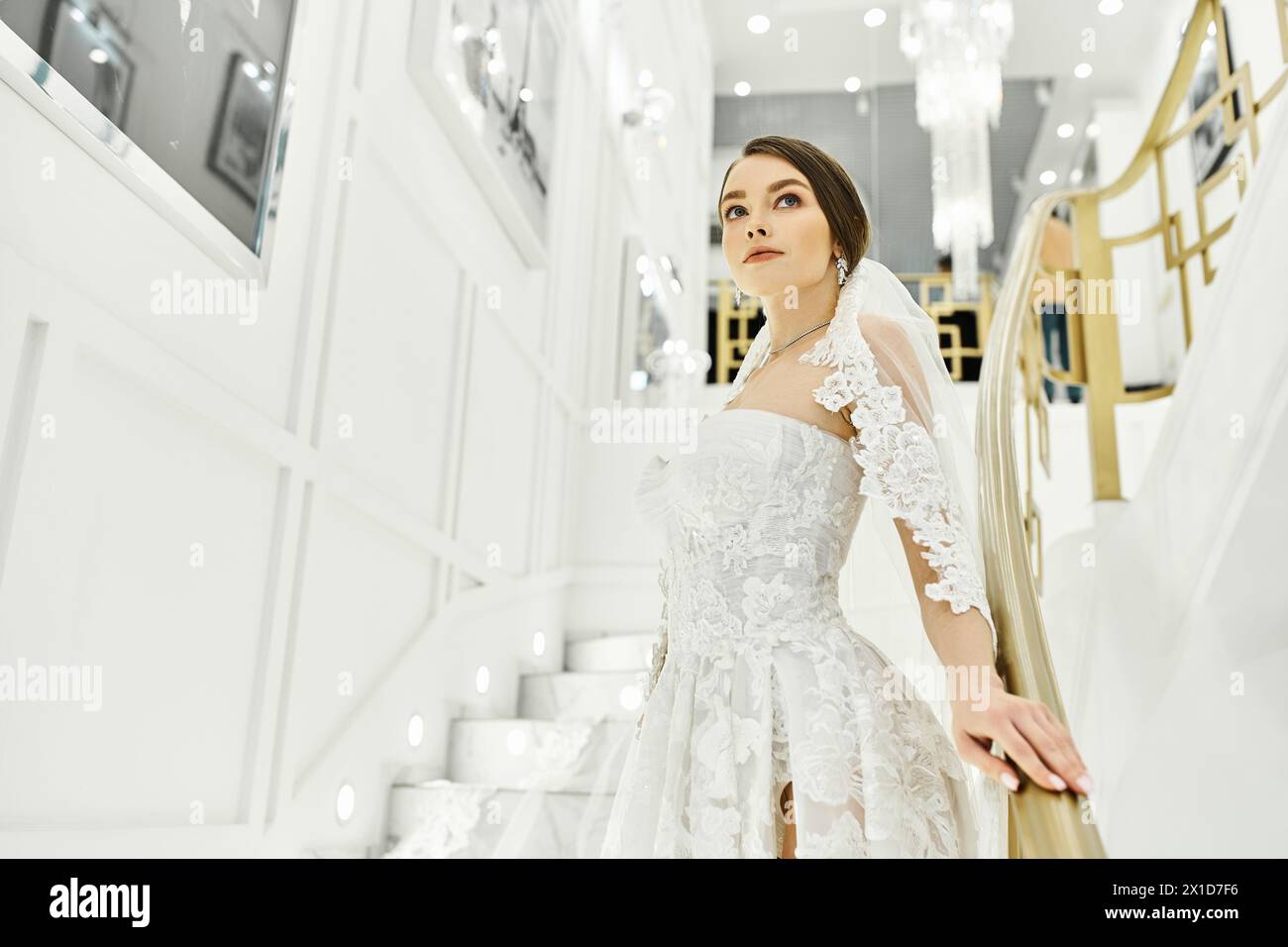 A young brunette bride in a wedding dress stands on a staircase in a bridal salon. Stock Photo