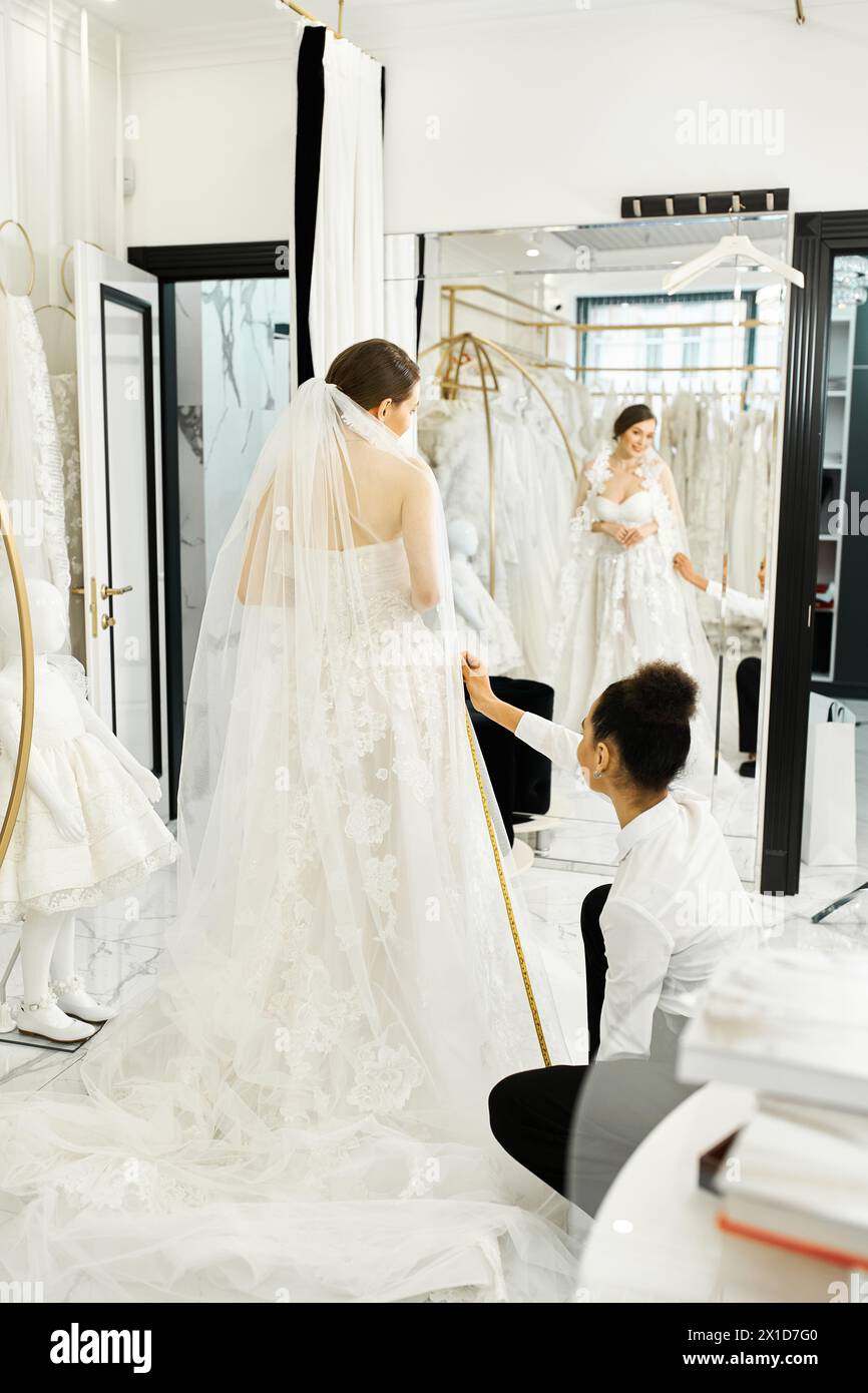 A young bride in a white wedding gown converses with an African American shopping assistant in a luxurious bridal salon. Stock Photo