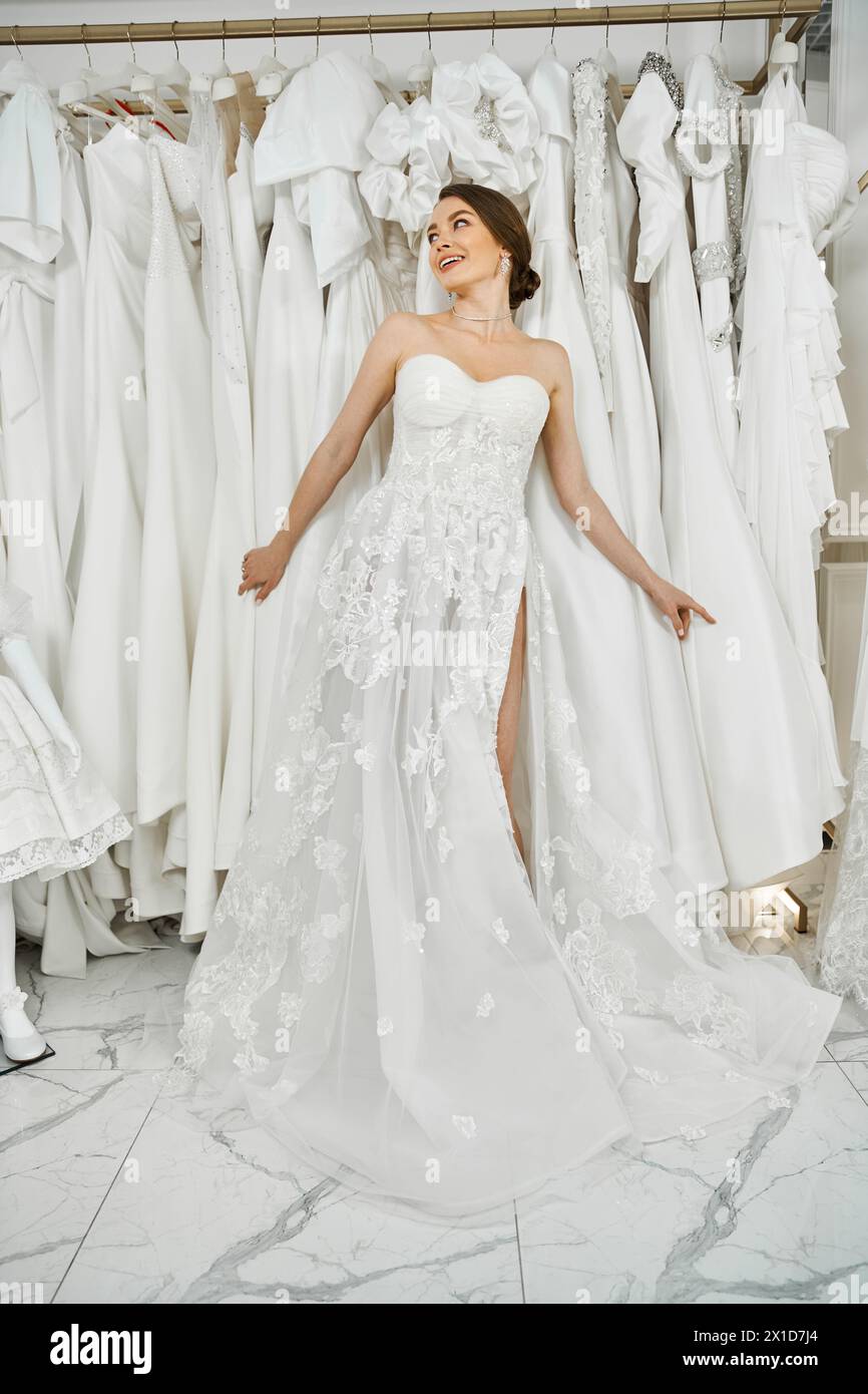 A young, beautiful bride admires a rack of dresses in a wedding salon, contemplating her perfect gown. Stock Photo