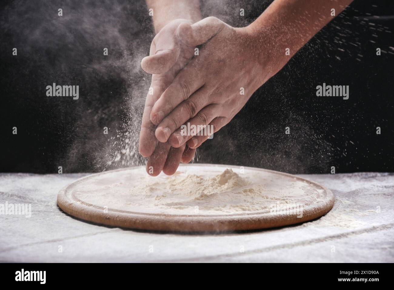 A male chef claps his hands filled with white flour on a black ...