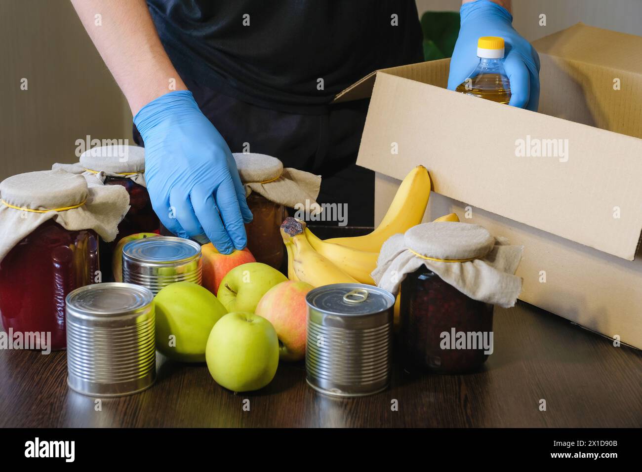 A volunteer wearing protective medical gloves puts food in a donation ...