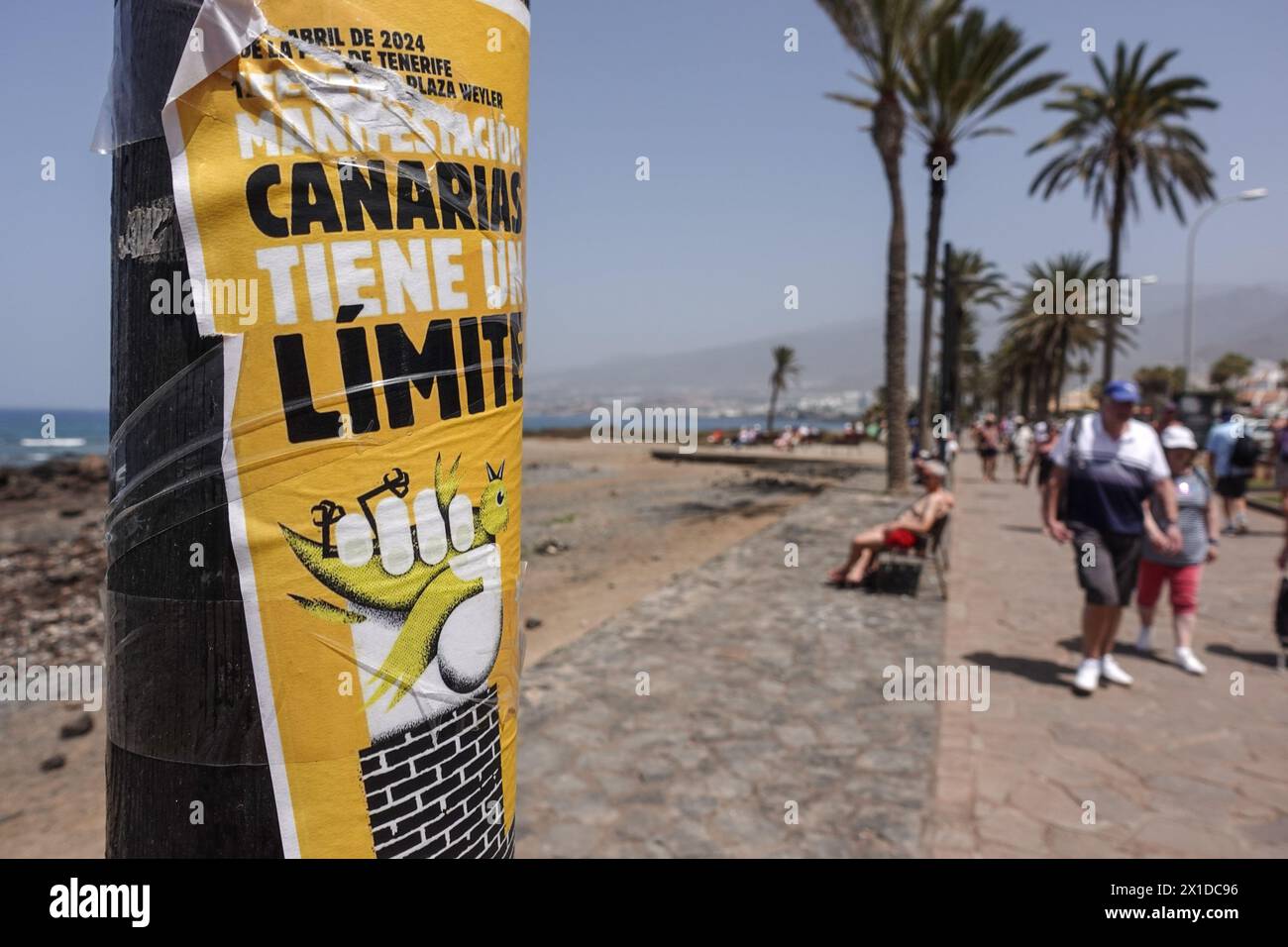 Los Cristianos, Tenerife, April 16th 2024 - Tourists walk past Anti-Tourist posters along the beach front in Los Cristianos. The poster reads that 'Canary Islands Have a Limit' the yellow signs advertise the anti-tourist protest on Saturday 20th April. in Santa Cruz de Tenerife. Parking is also a big problem in the area as hordes of visitors fill thousands of spaces, causing a headache for residents and visitors alike. Credit: Stop Press Media/Alamy Live News Stock Photo
