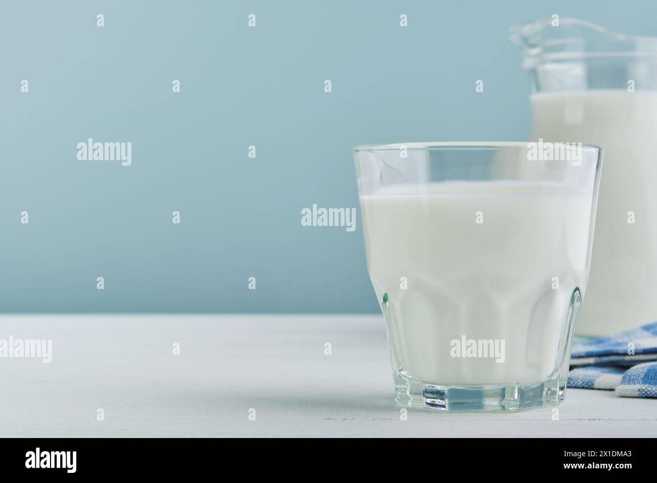 Milk in jug and glass on wooden table and blue background. Concept of farm dairy products, milk day. Kitchen or supermarket mock up for design. Copy s Stock Photo