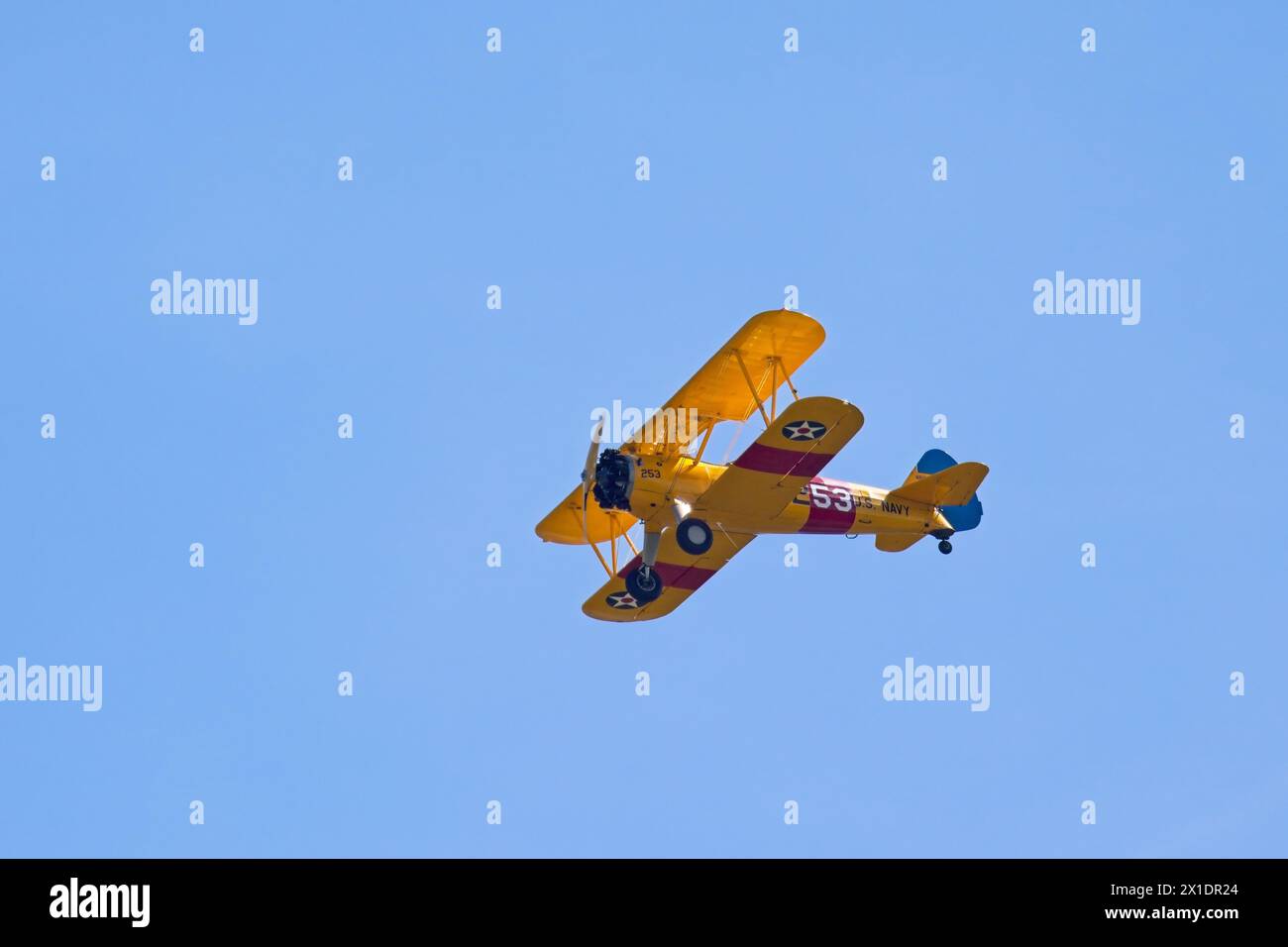 A yellow old style biplane soars up in the bright blue sky near Liberty