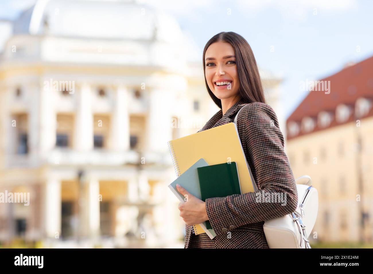 Smiling student holding books in front of building Stock Photo - Alamy