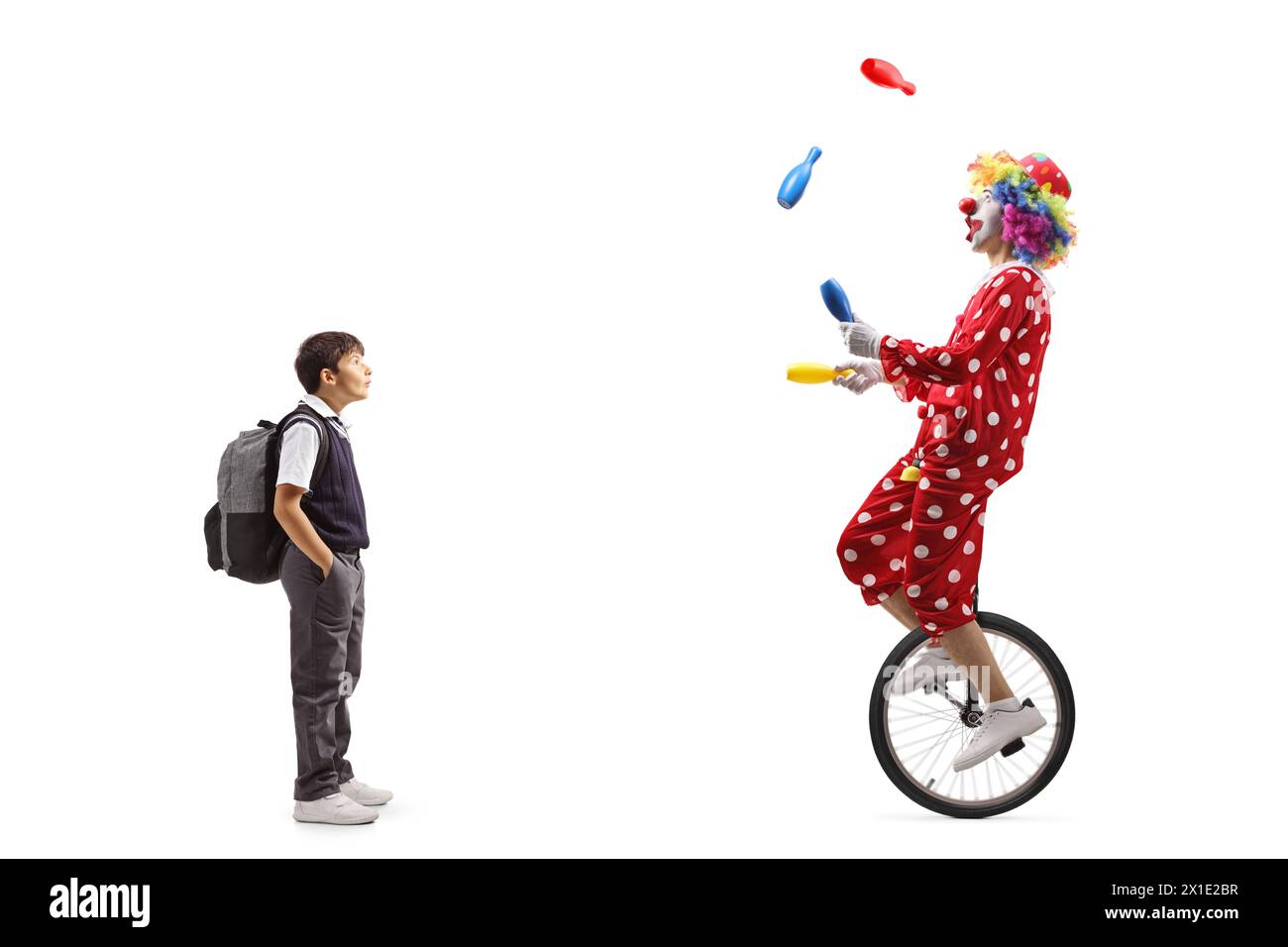 Full length shot of a surprised schoolboy looking at a clown juggling ...
