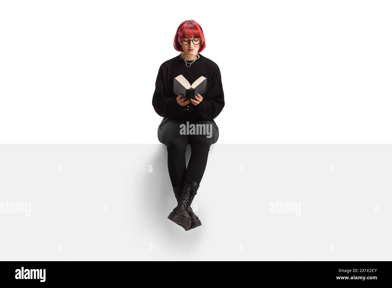 Woman with red hair sitting on a blank panel and reading a book ...