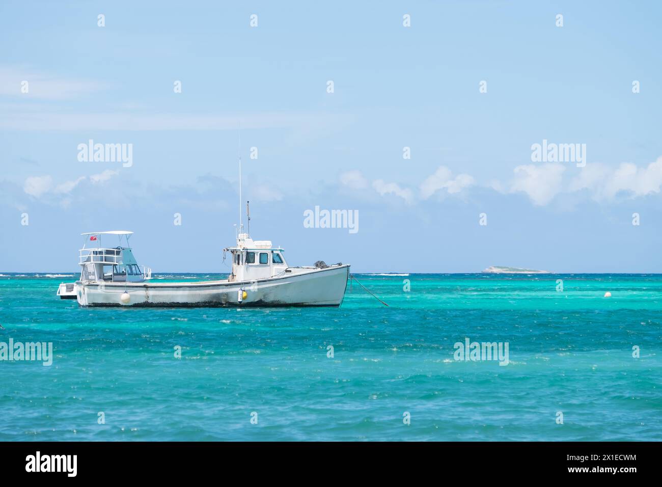 A small white boat is floating in the ocean. The sky is clear and blue, and the water is calm Stock Photo