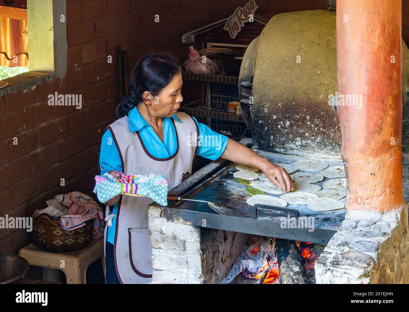 An old woman cooking corn tortilla on traditional flat topped stove