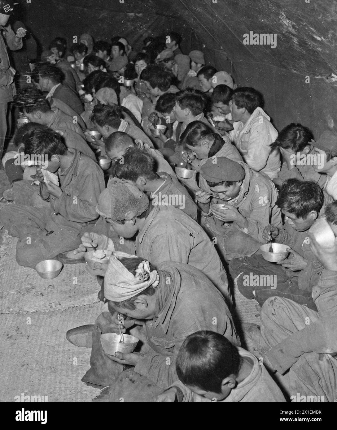 Communist guerrillas and their families, captured and brought down from Mount Chirisan, by elements of the Republic of Korea Capitol Division, are fed in the Prisoner of War stockade, Kurije, Korea ca. Decmeber 1951 Stock Photo