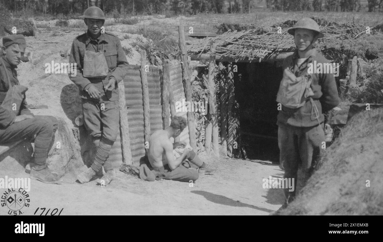 A member of the 166th Infantry picks cooties out of his shirt at the door of a dugout near 2nd line trenches west of Suippes France ca. 1918 Stock Photo