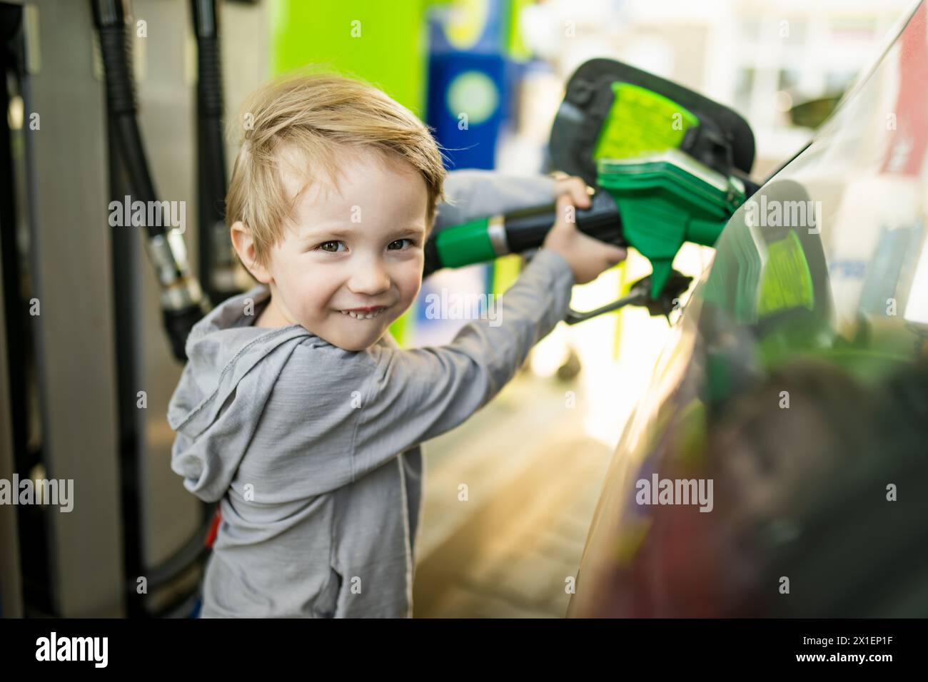 Cute little blond boy holding pump nozzle. Small funny kid helping