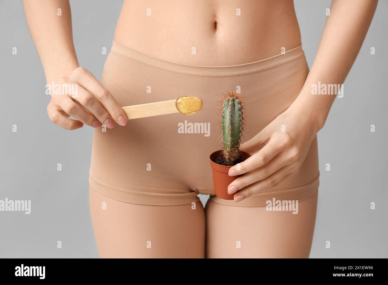 Beautiful young woman holding cactus and spatula with sugaring paste on grey background, closeup Stock Photo