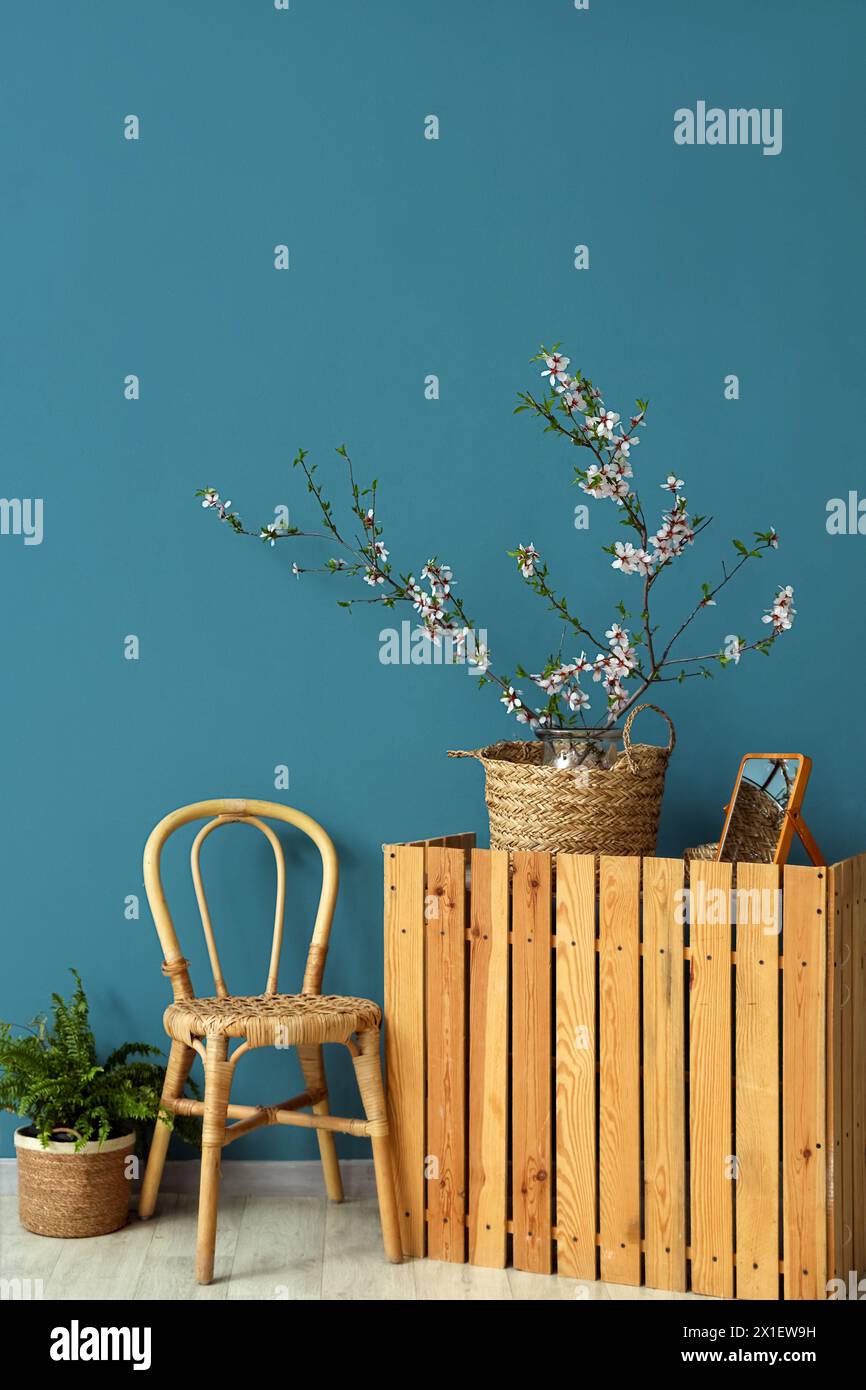 Minimalist interior with wooden furniture, wicker basket and blooming branches near blue wall Stock Photo