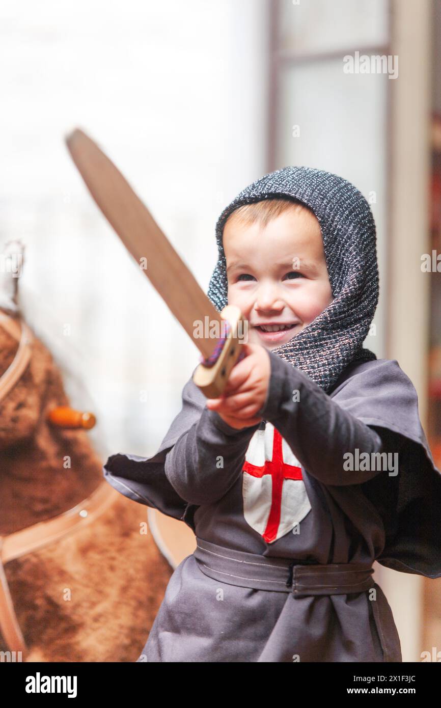 Little boy dressed as a knight happily plays with a wooden sword with a ...