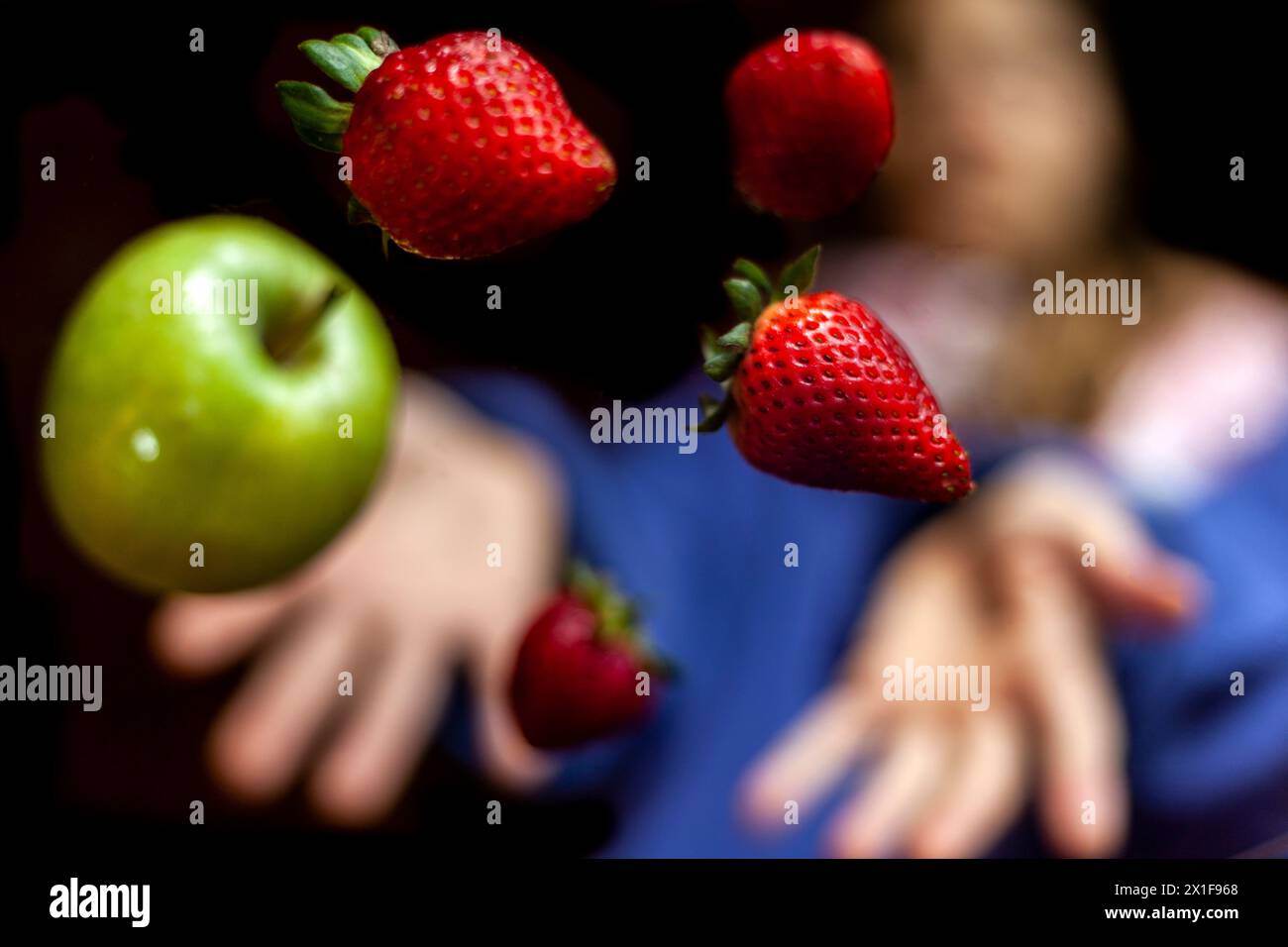 Unfocused hands throw Green apple and strawberries in the air with black background. Nutrition concept Stock Photo