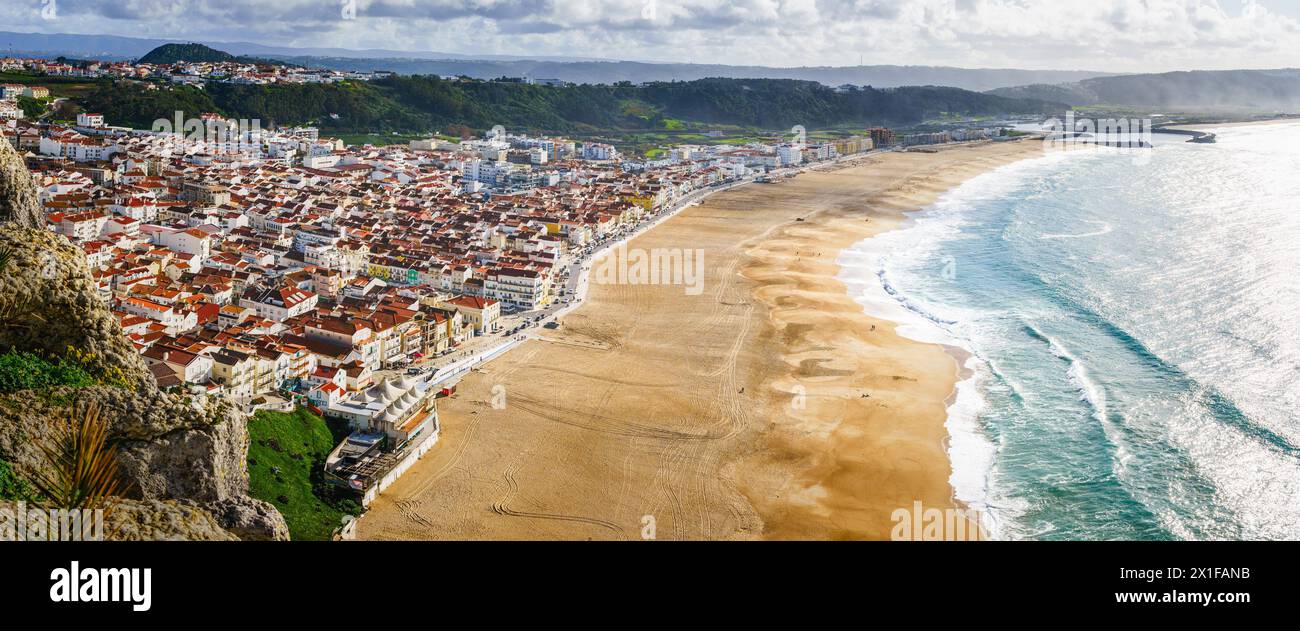Overlooking the sweeping curve of Nazare's shoreline, where the sun kisses the Atlantic. Panoramic view Stock Photo