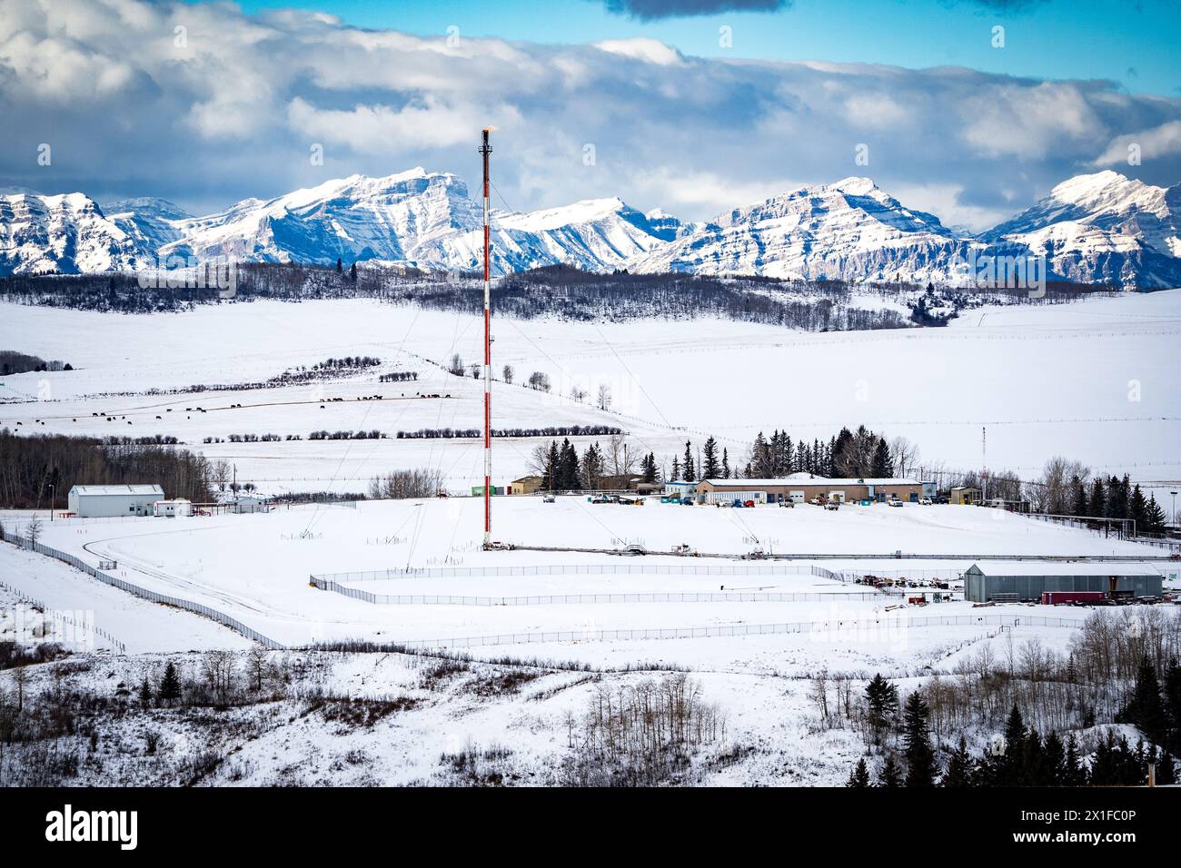 Oil and gas industry flare stack overlooking snow covered hills with Alberta Rocky Mountains at background in Western Canada. Stock Photo