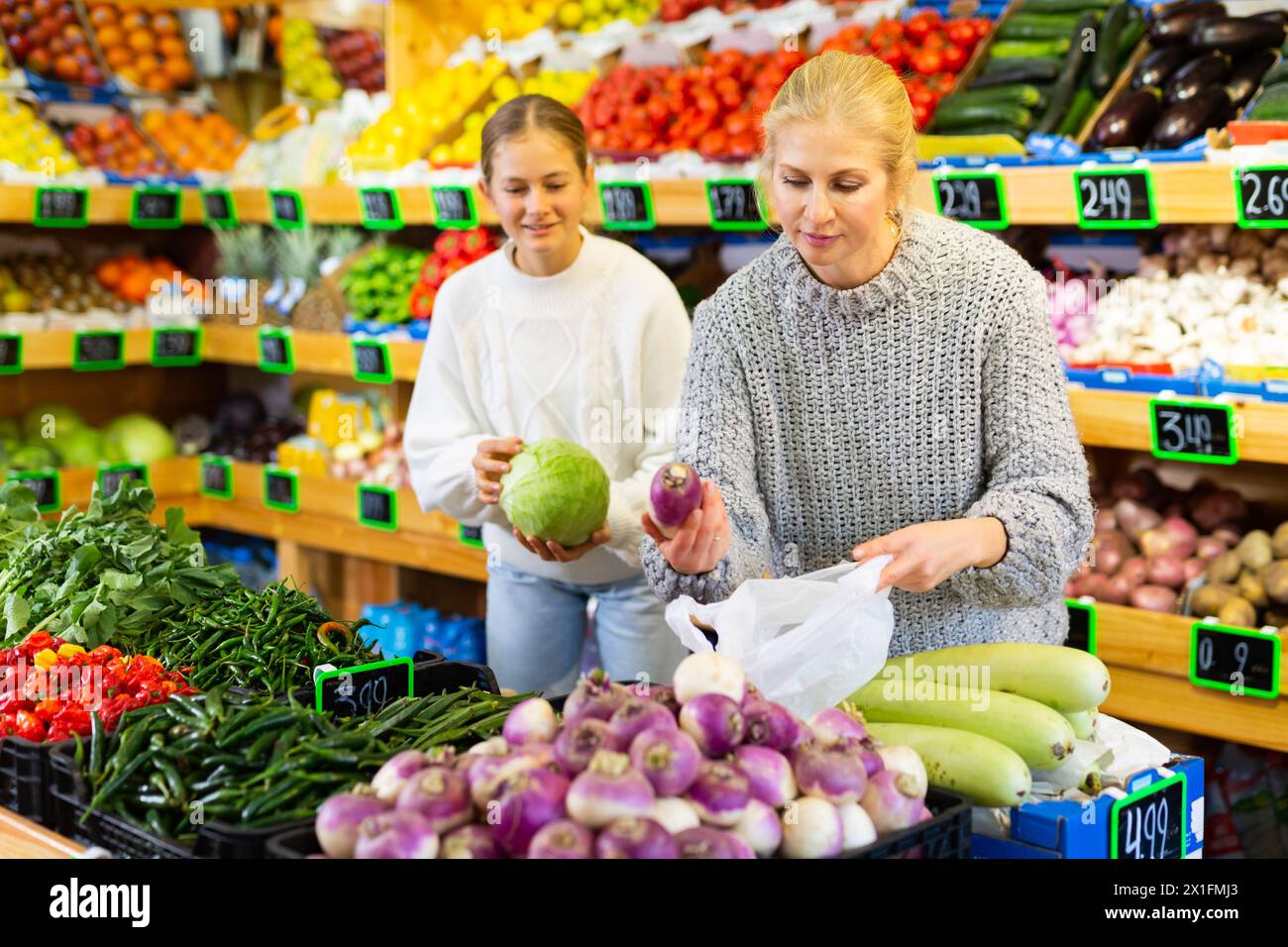 Portrait of teenage girl and her mother who buying fresh vegetables and ...