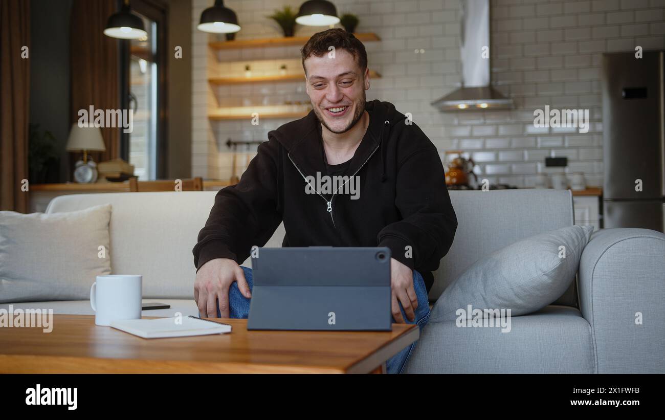 Man sit on the sofa having video call conversation through using tablet computer at home. Share news, talk to family or friends, enjoy online video ch Stock Photo