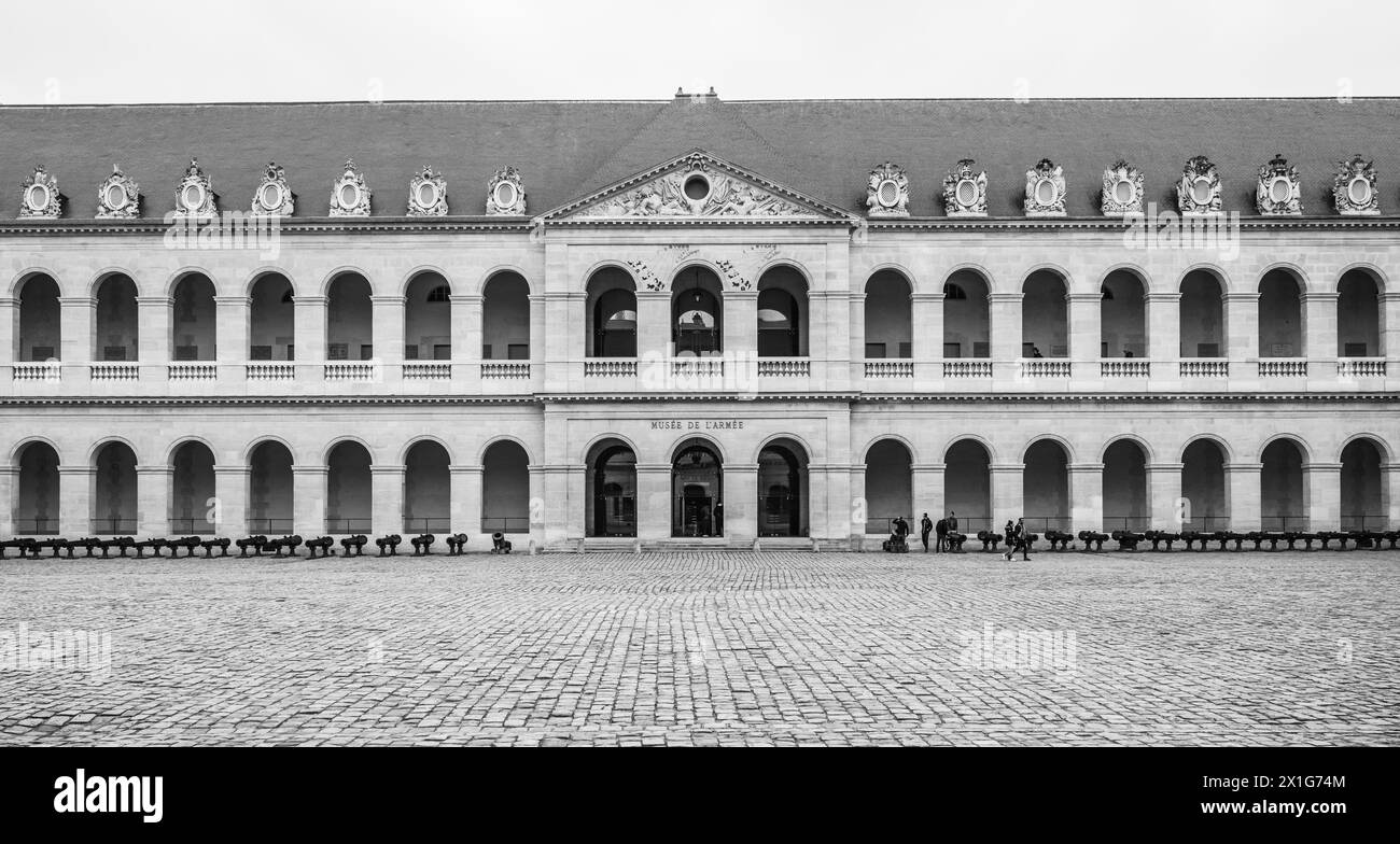 Visitors walk across the cobblestone courtyard of Les Invalides under an overcast Paris sky, France. Black and white image. Stock Photo