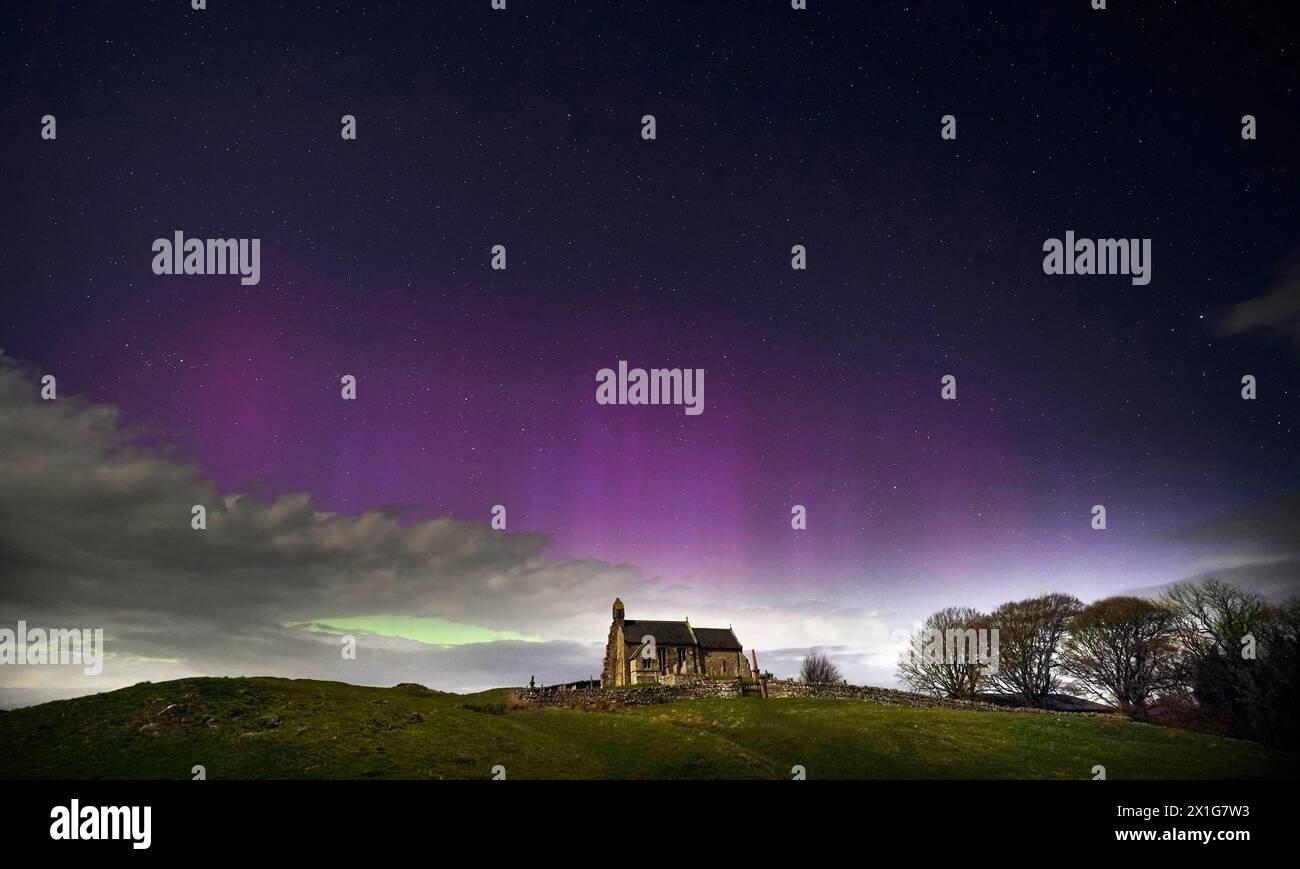 The aurora borealis, also known as the Northern Lights, illuminate the sky just before midnight over St Aidan's church in Thockrington, Northumberland. Picture date: Wednesday April 17, 2024. Stock Photo