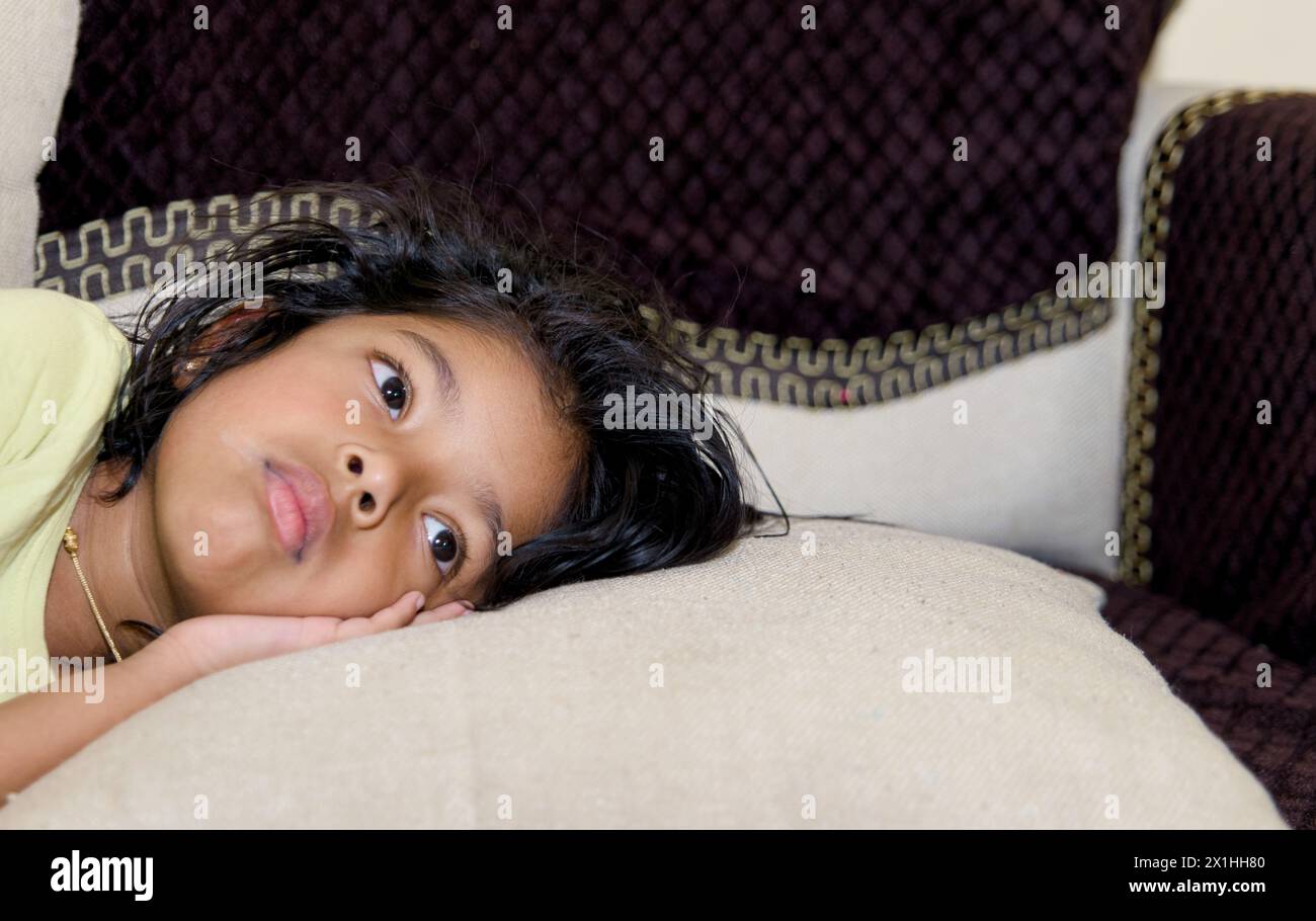 This image is about little asian girl sadly lying on the sofa in the living room at home Stock Photo
