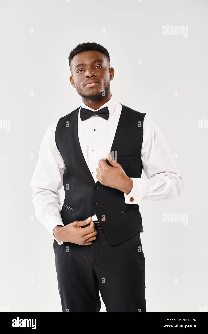 A young African American man in a stylish tuxedo strikes a sophisticated pose for a portrait on a gray studio background. Stock Photo