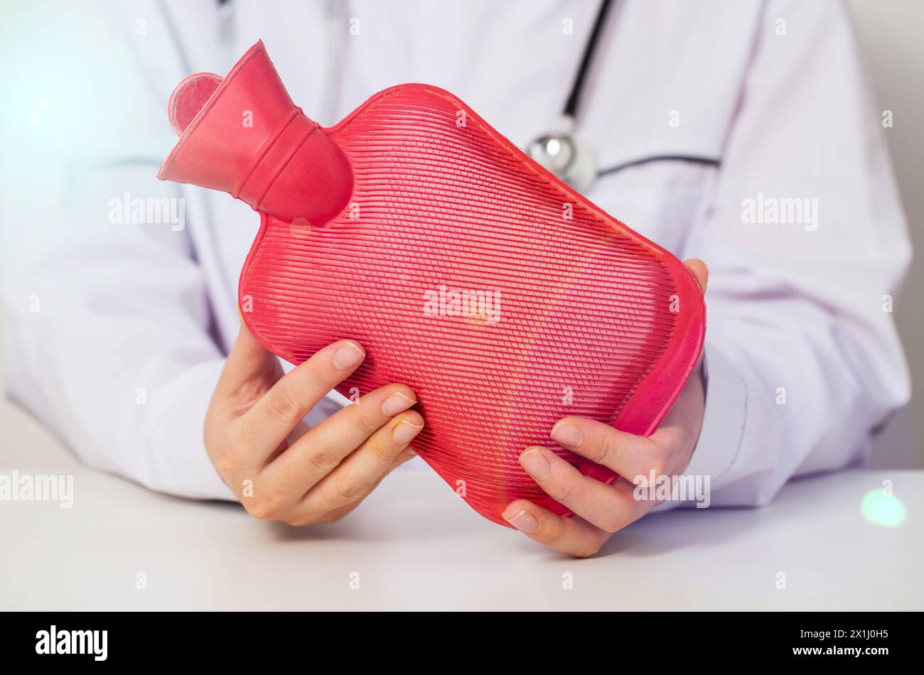 The doctor is holding a red heating pad with hot water in his hands. The concept of heat treatment, muscle relaxation, spasm relief. Stock Photo