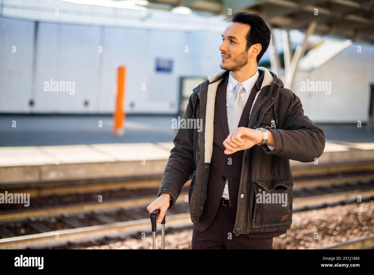 Young man in a suit checks his watch while waiting for the train, displaying urgency and time management Stock Photo