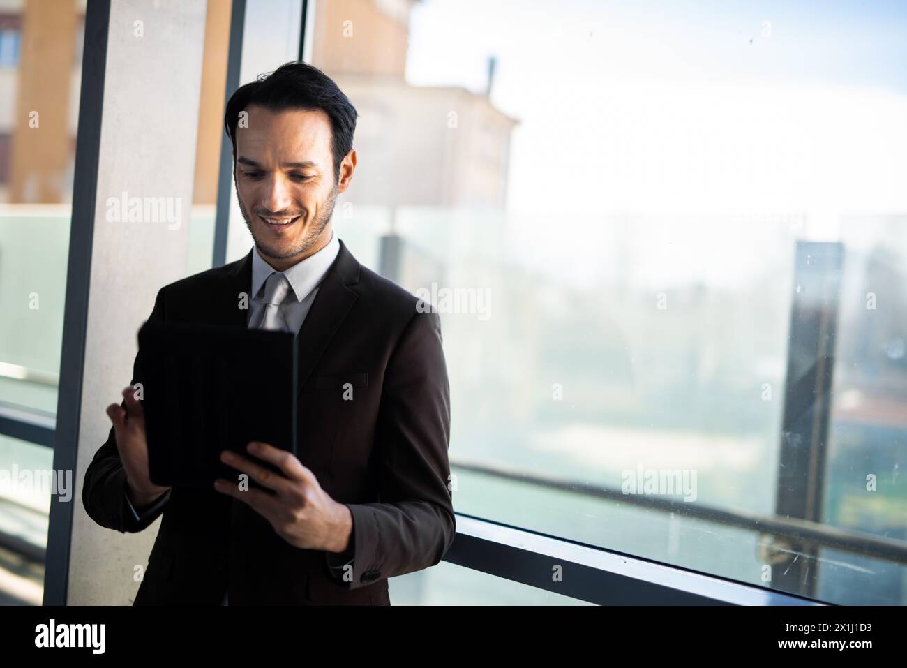 Professional male in suit engages with technology by a window with natural light Stock Photo