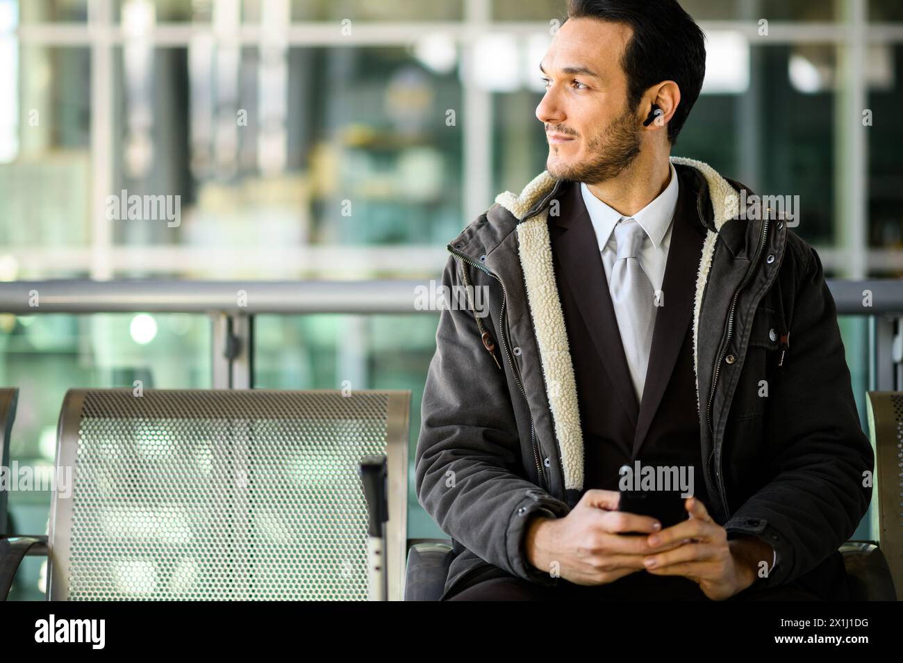 Young adult male in professional attire using a phone while sitting at a public transport station Stock Photo