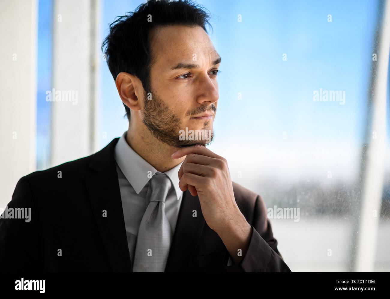 Professional male in a suit looks contemplatively out of an office window Stock Photo