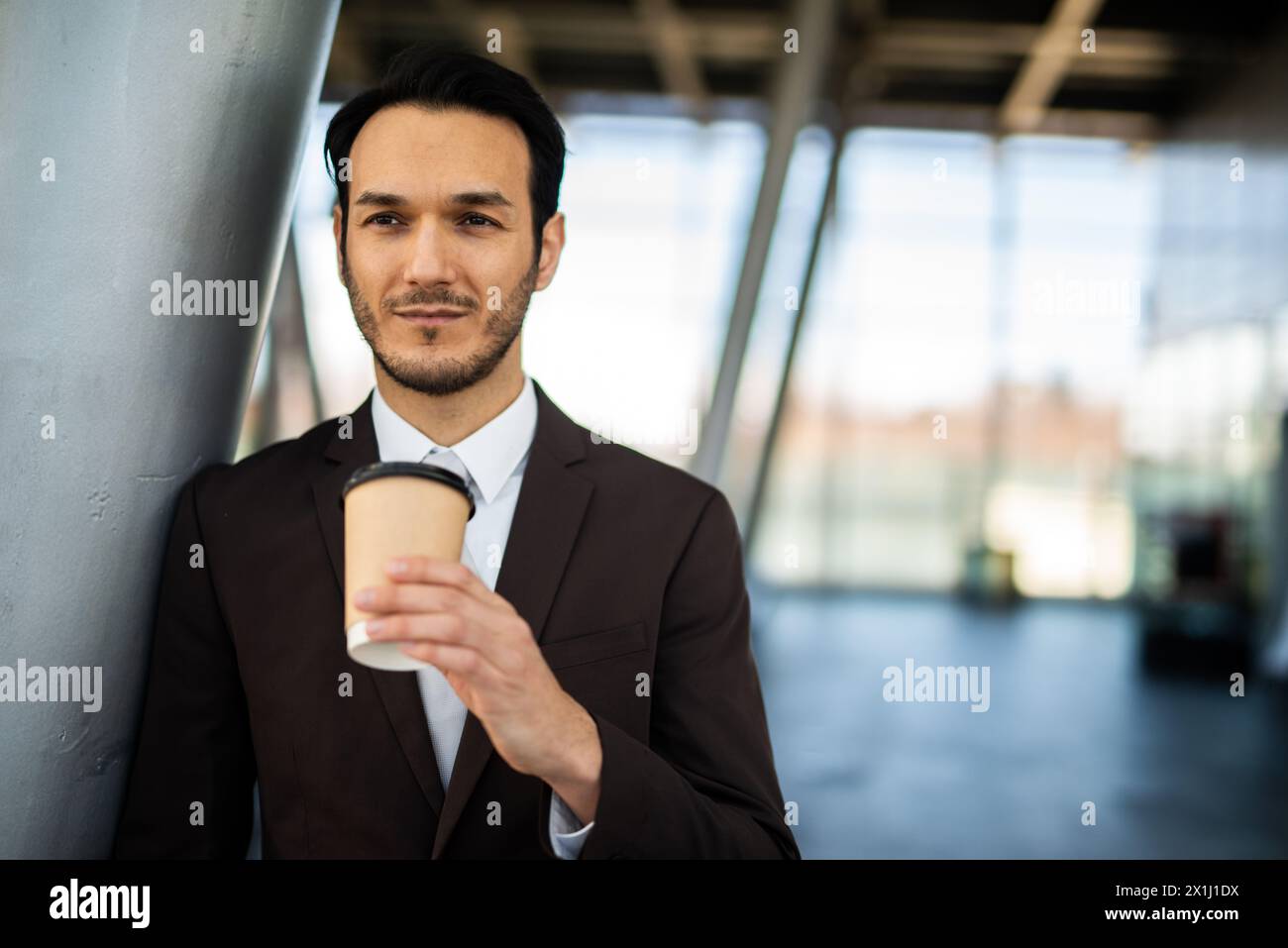 Professional young man in a suit holding a coffee cup in a bright office setting Stock Photo