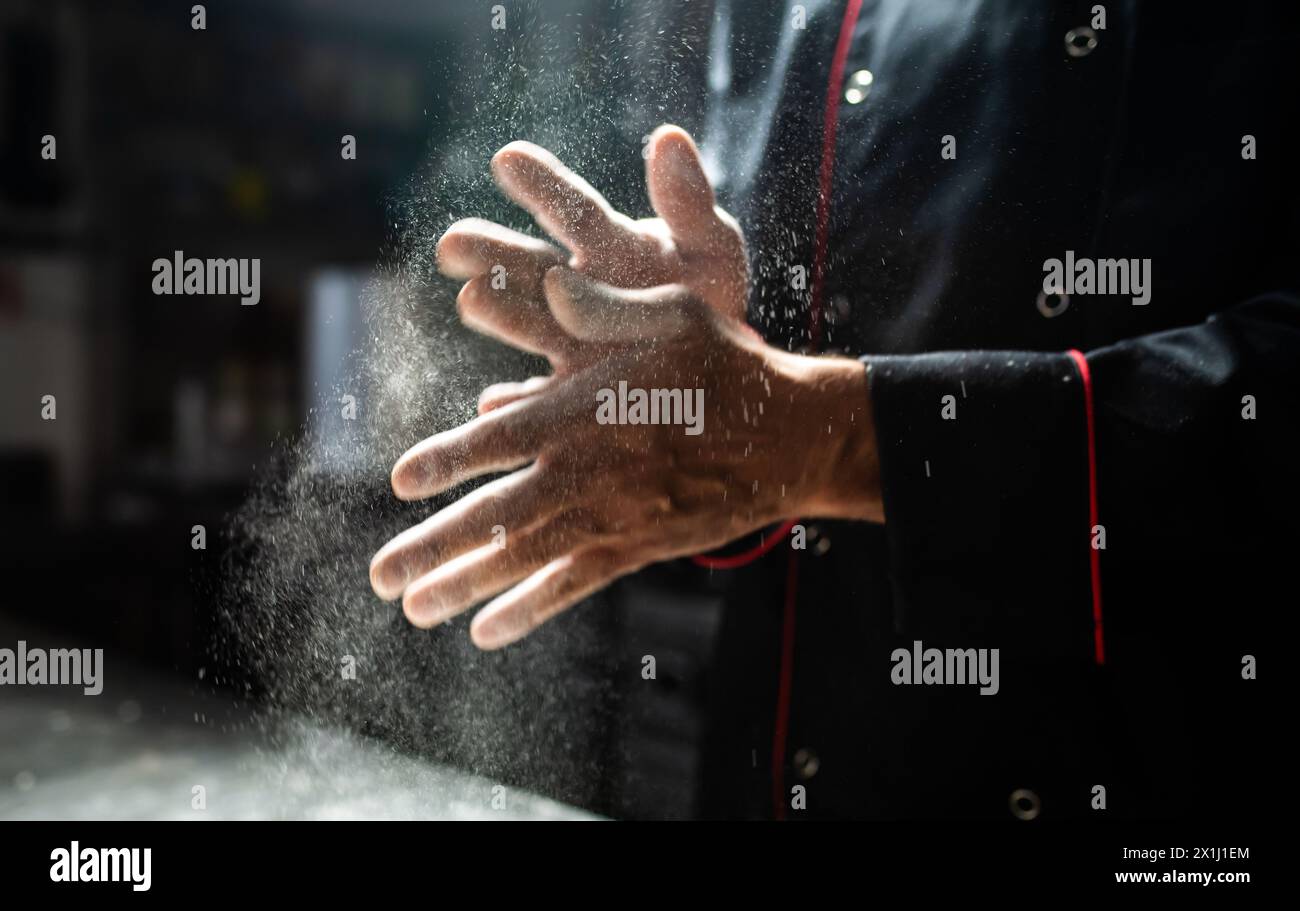 Close-up of a chef's hands with flour dusting through sunbeams Stock Photo