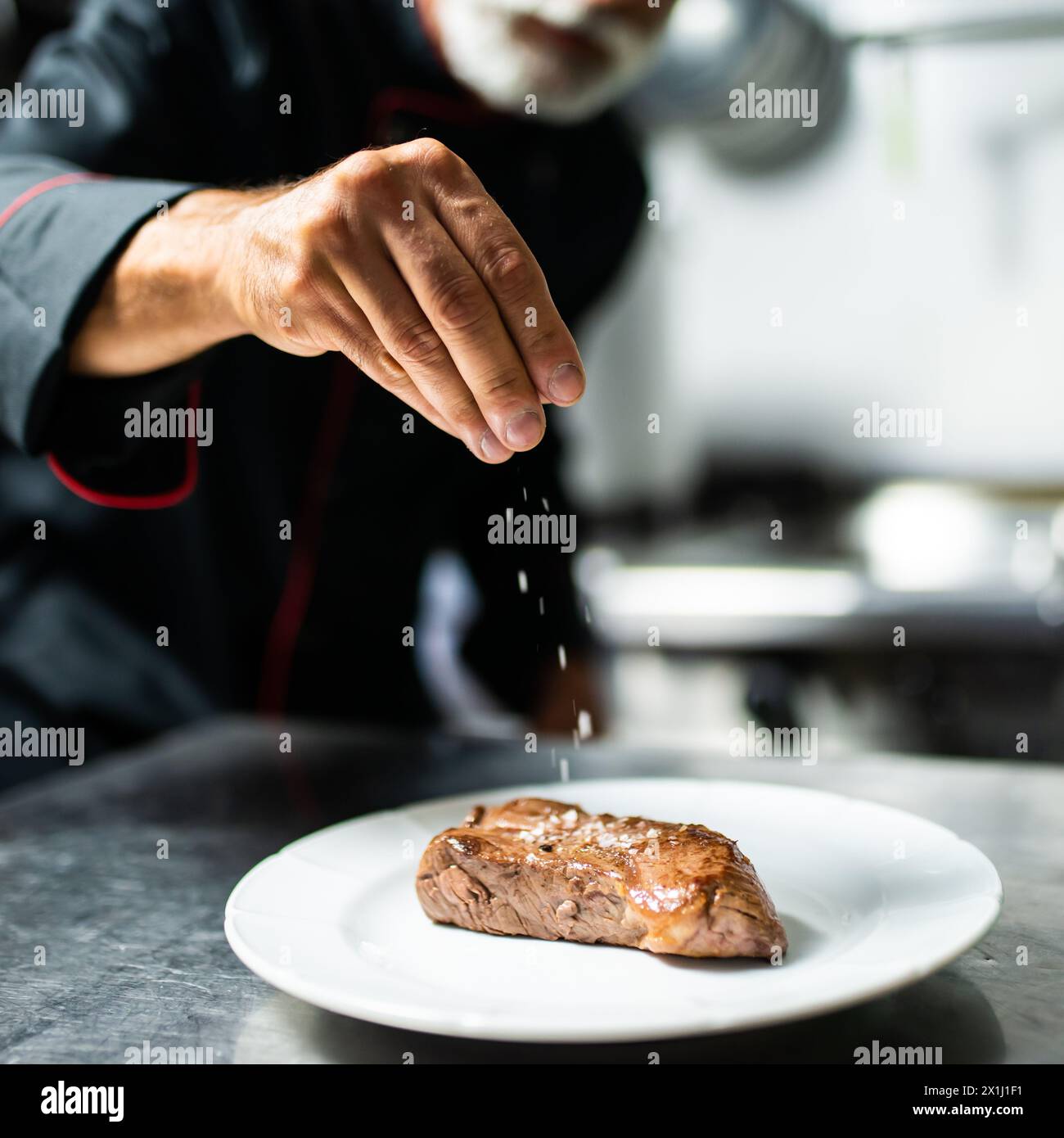 Close-up of a chef's hand sprinkling salt on a grilled steak Stock Photo
