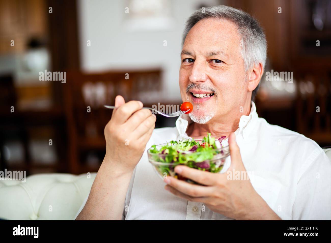 Smiling mature man savors a healthy bowl of salad indoors Stock Photo