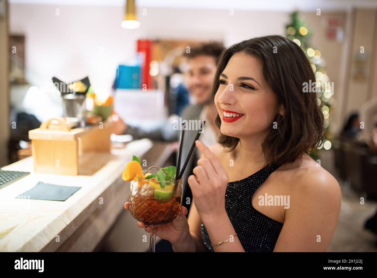Young woman drinking a cocktail at a bar counter Stock Photo