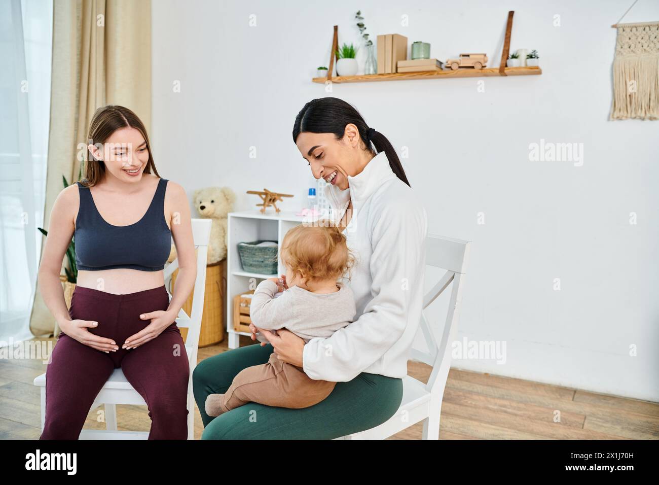 A young, beautiful mother sits in a chair holding her baby while receiving guidance from her parenting coach. Stock Photo
