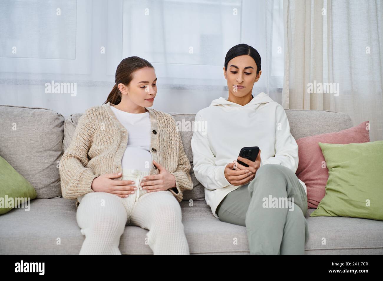 A pregnant woman and her trainer sit comfortably on top of a couch