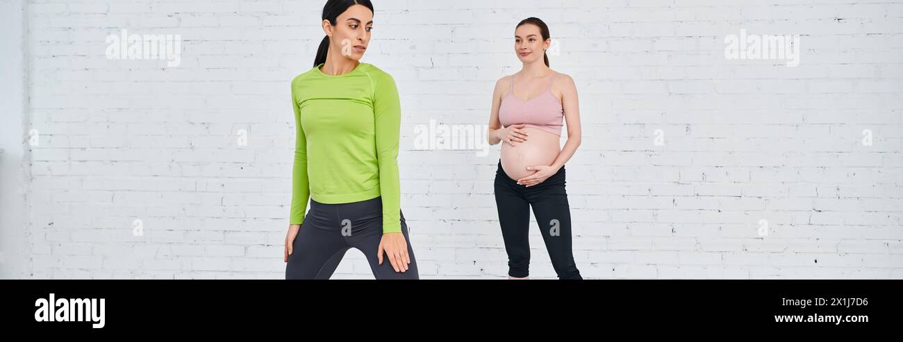 A woman stands strong next to a pregnant woman during a parents course, supporting and guiding her through exercises. Stock Photo