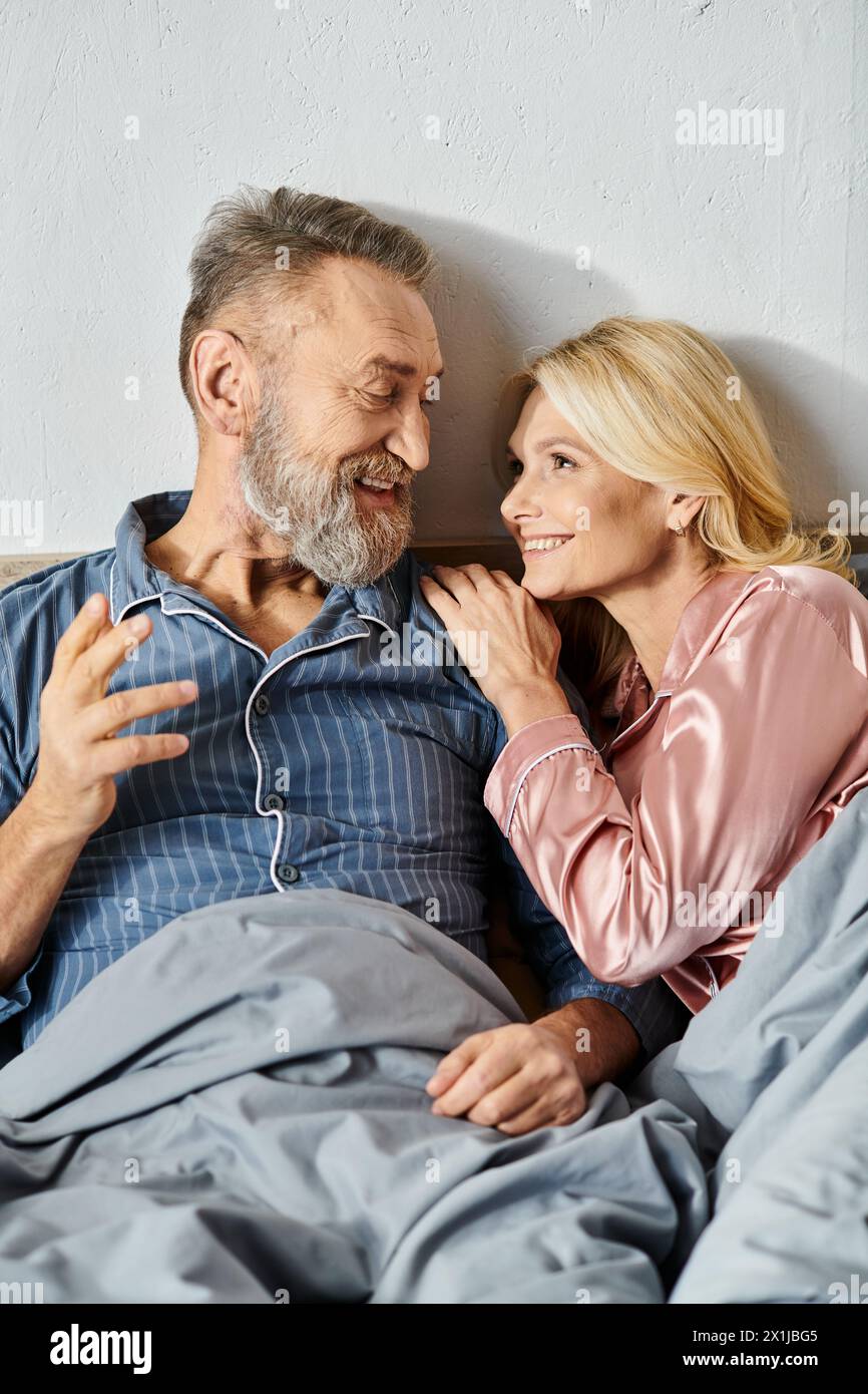 A mature loving couple, dressed in cozy homewear, peacefully laying together in bed, enjoying each others company. Stock Photo