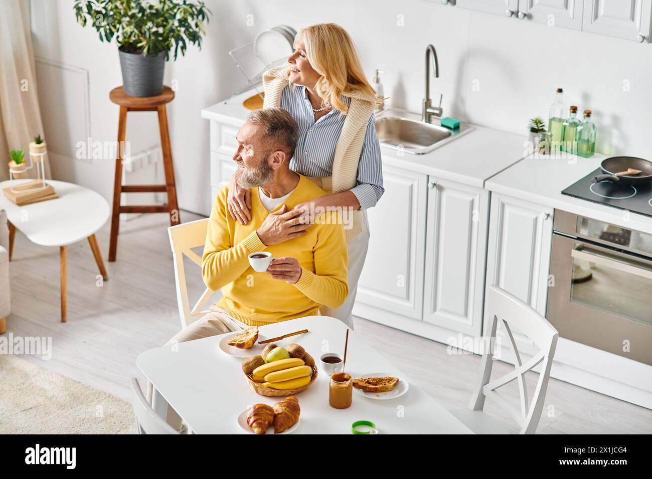 A man and a woman, a mature loving couple, sitting in chairs together, enjoying each others company in cozy homewear at home. Stock Photo