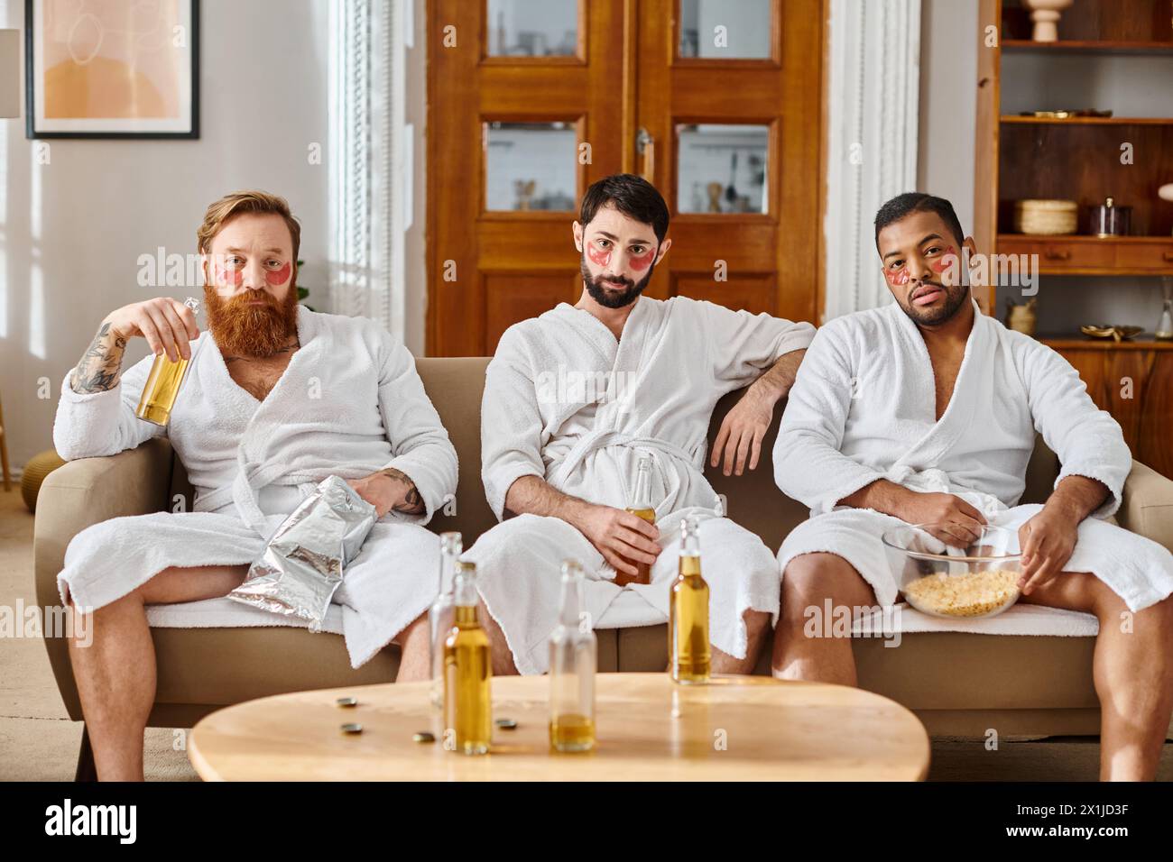 Three diverse, cheerful men wearing bathrobes, sitting on top of a couch, enjoying a great time together. Stock Photo