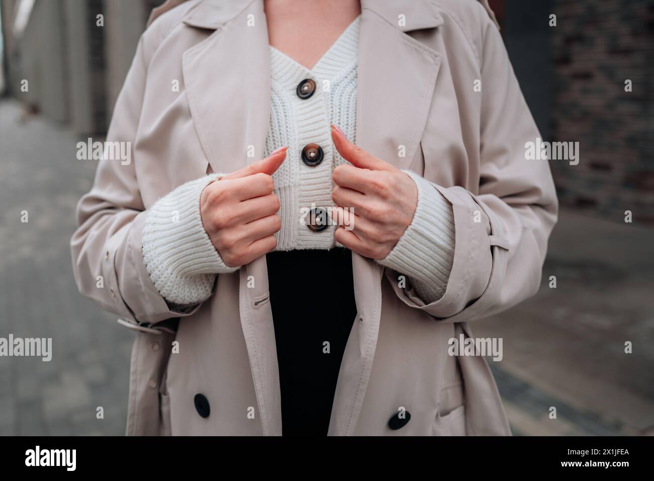 Street style fancy details of a knitted white button-up sweater and beige women's trench coat. Contemporary urban fashion Stock Photo