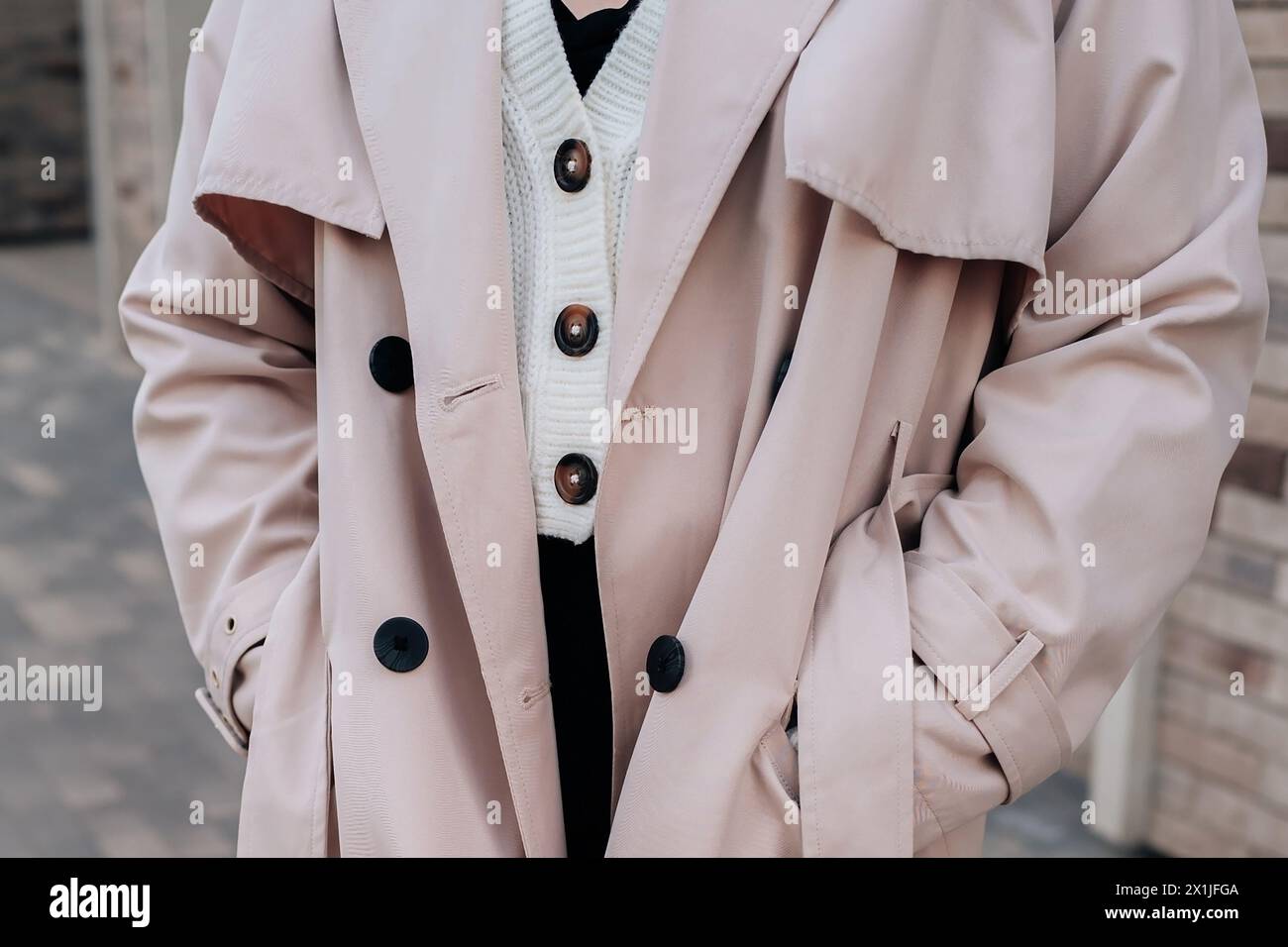 Street style fancy details of a knitted white button-up sweater and beige women's trench coat. Contemporary urban fashion Stock Photo